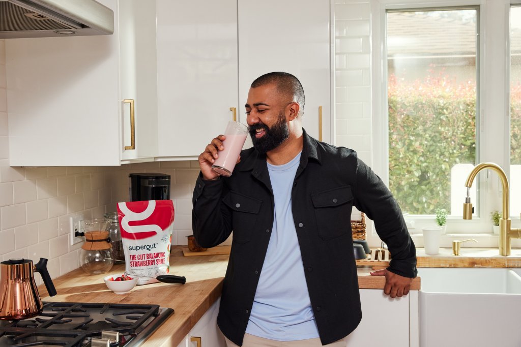 A man drinking a Supergut shake in a kitchen